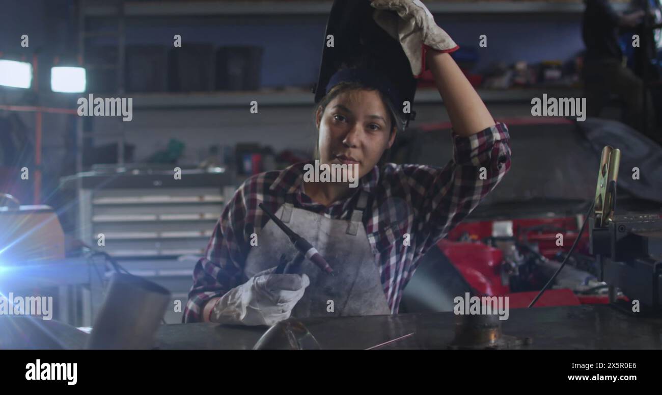 A young biracial woman is working in workshop, holding a welding tool Stock Photo
