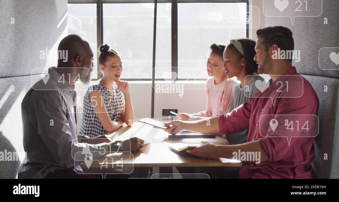 Anmation of social media icon floating over team of diverse colleagues discussing together at office Stock Photo