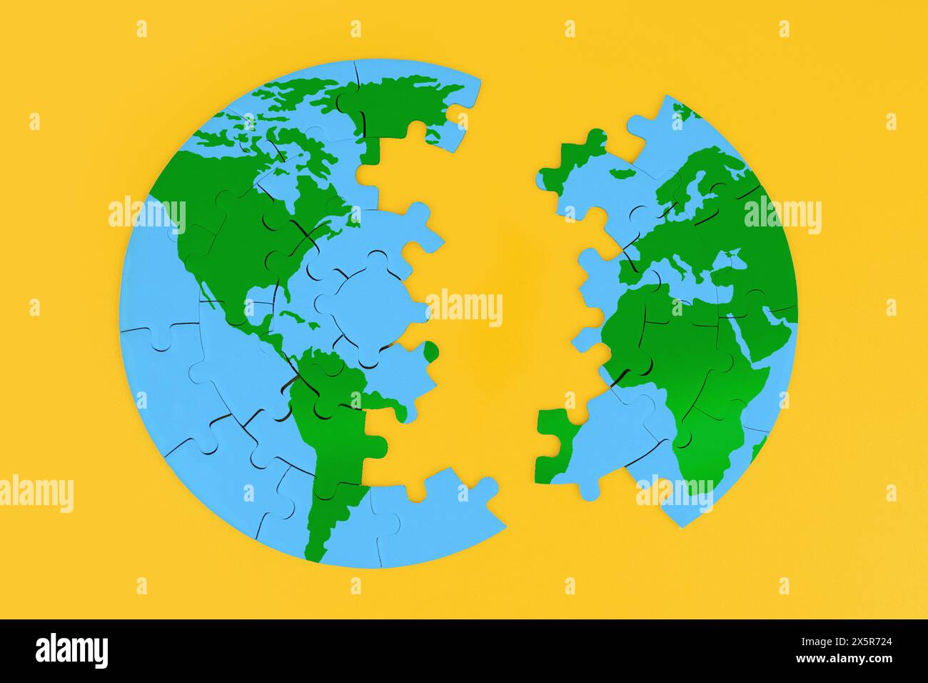 Jigsaw globe puzzle with green continents and blue oceans split into two parts against a bold yellow backdrop. Unity, division and global interconnect Stock Photo