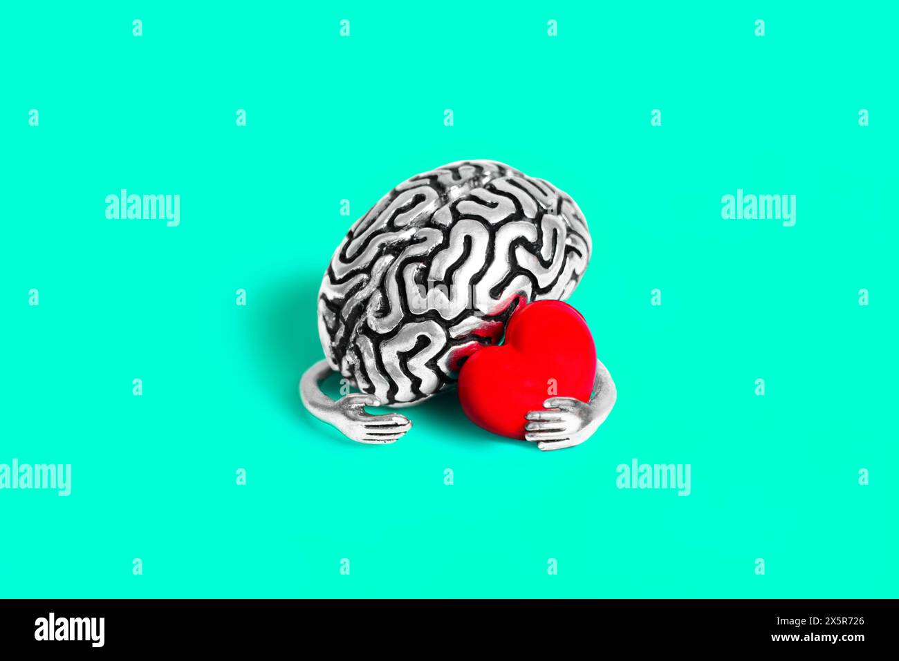Anatomical model of a human brain with cute hands made of steel gently holds a red heart isolated on teal background. Creative mind and feelings relat Stock Photo
