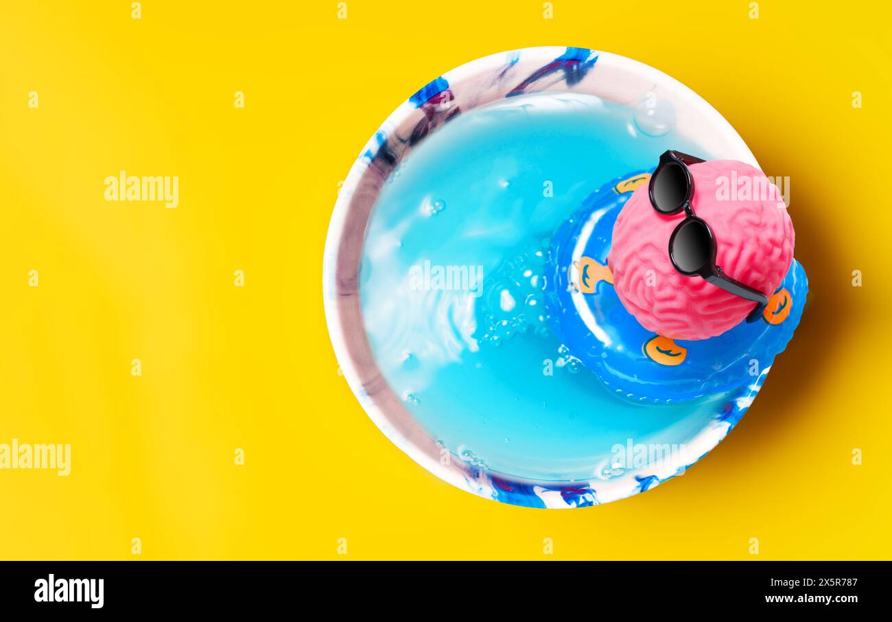 Pink brain in black sunglasses floats in a cup pool on an inflatable ring. Office escape and vacation concept. Stock Photo