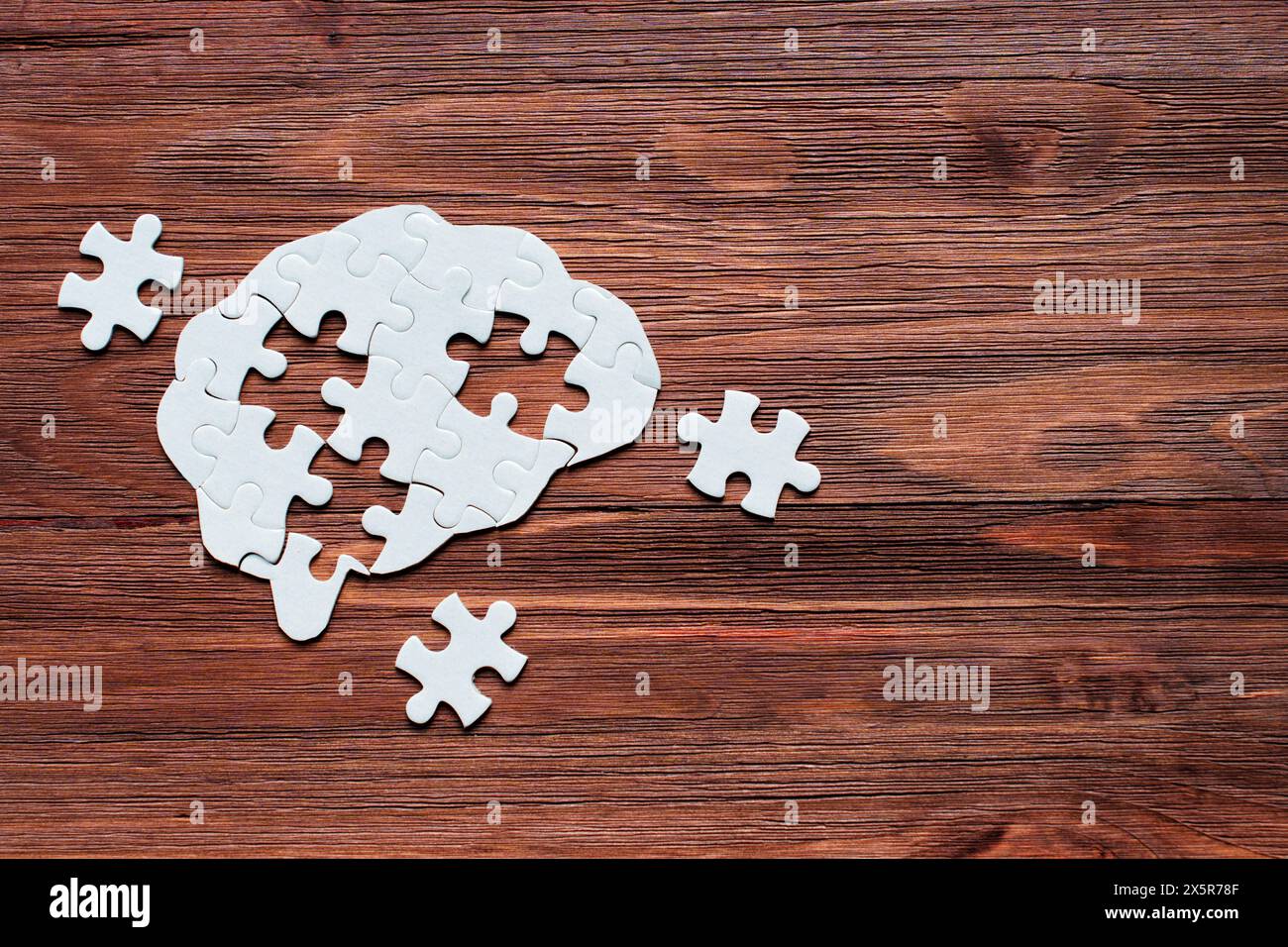 Human brain-shaped puzzle with several missing pieces lying nearby, set against a dark wooden background. Problem-solving and intellectual exploration Stock Photo
