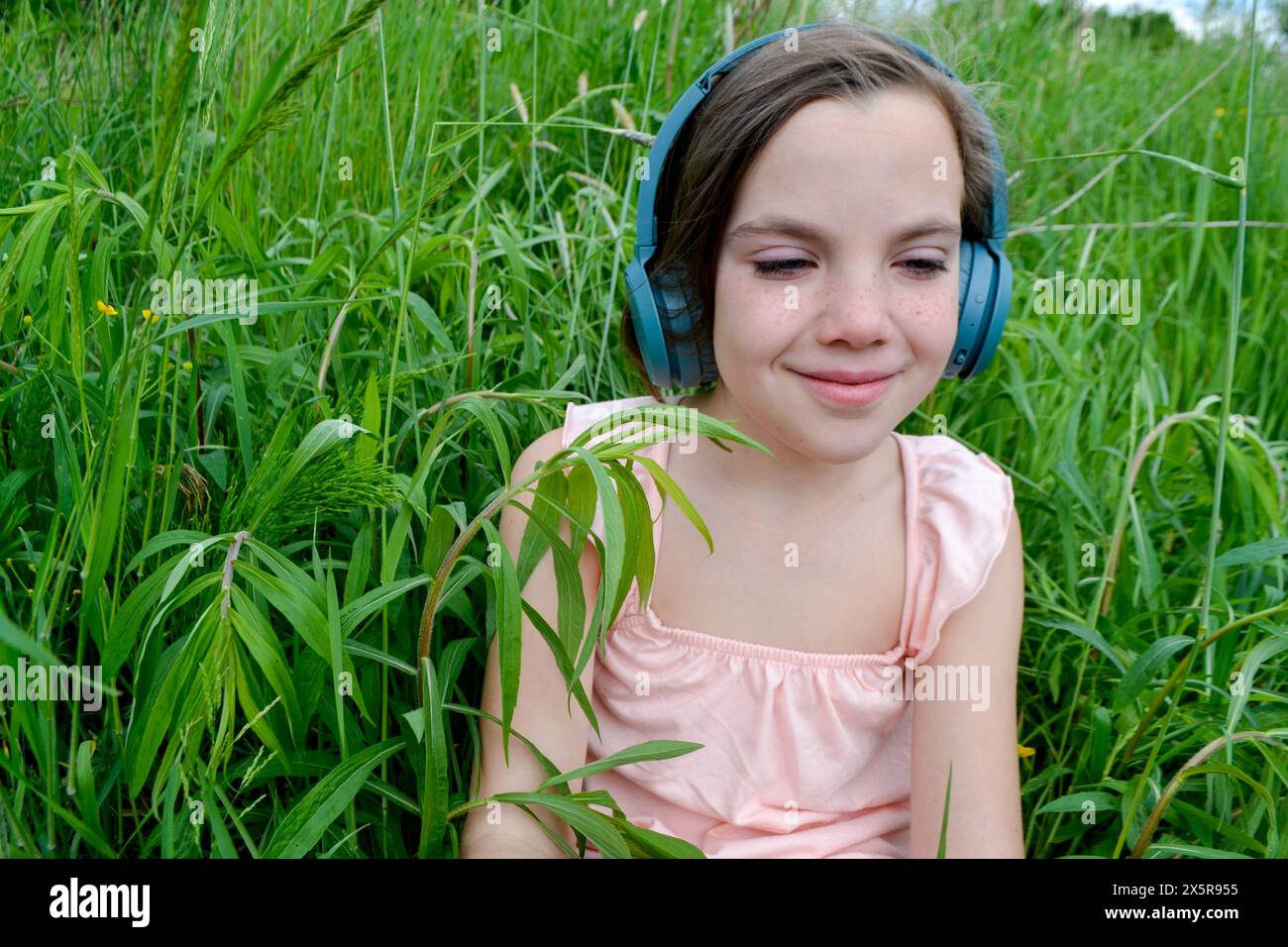 Relaxed woman lying on the grass listening to music with headphones in a park. Little girl listening to music in her headphones in the park on the gra Stock Photo