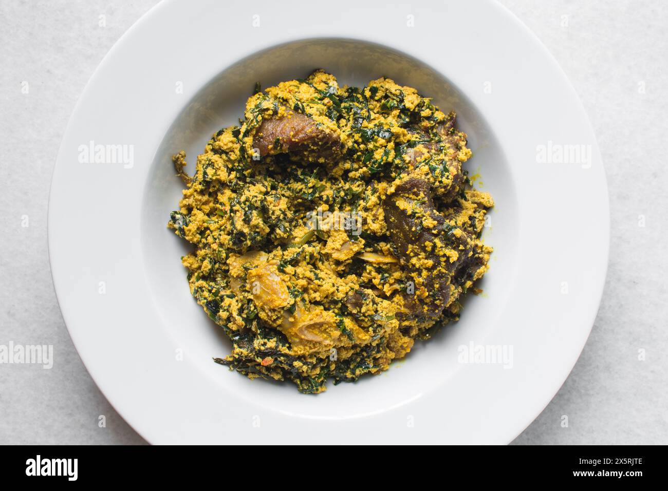 Nigerian egusi soup with fish and beef in a white plate, egusi vegetable soup in a large dinner plate Stock Photo