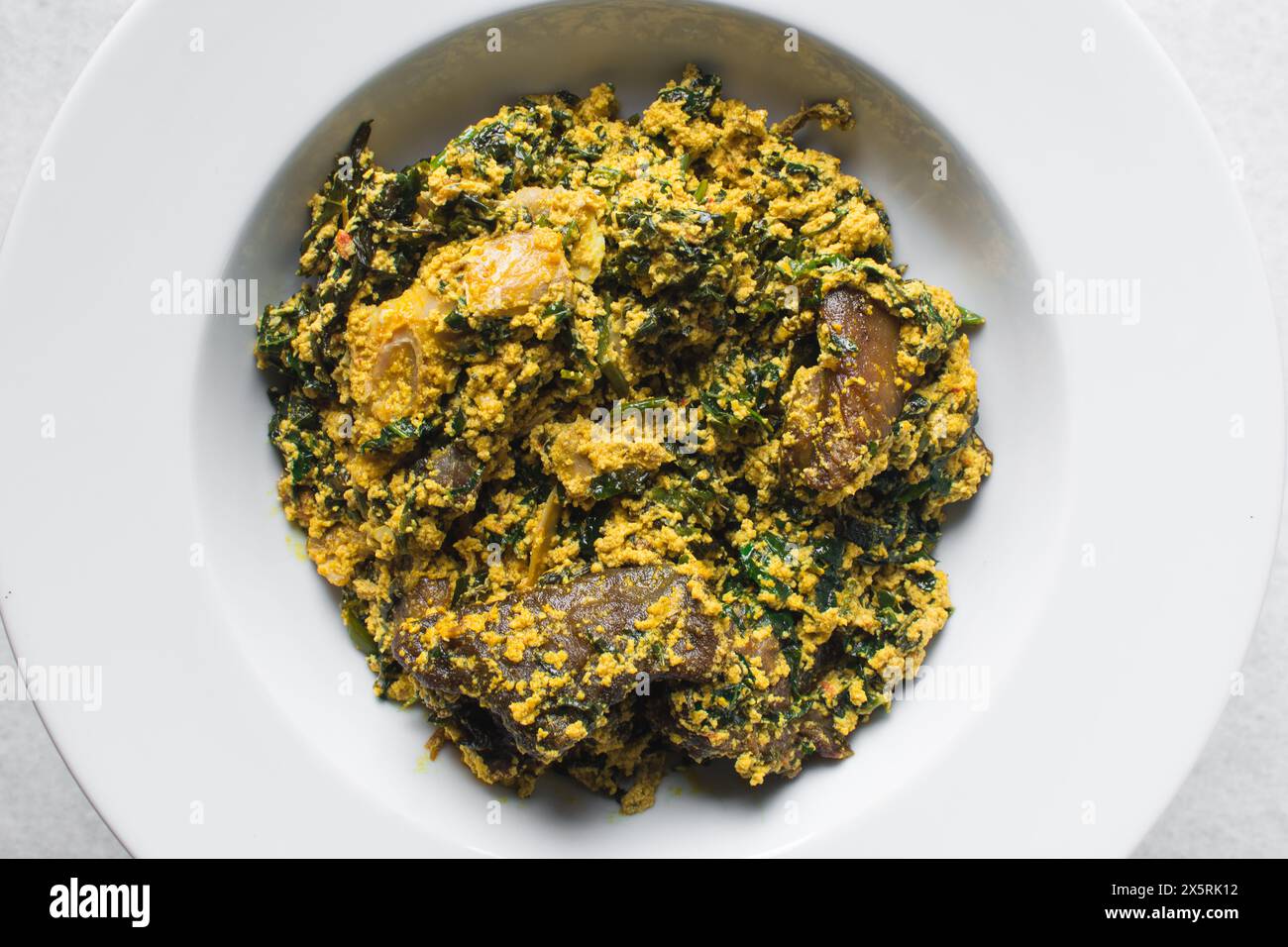 Nigerian egusi soup with fish and beef in a white plate, egusi vegetable soup in a large dinner plate Stock Photo