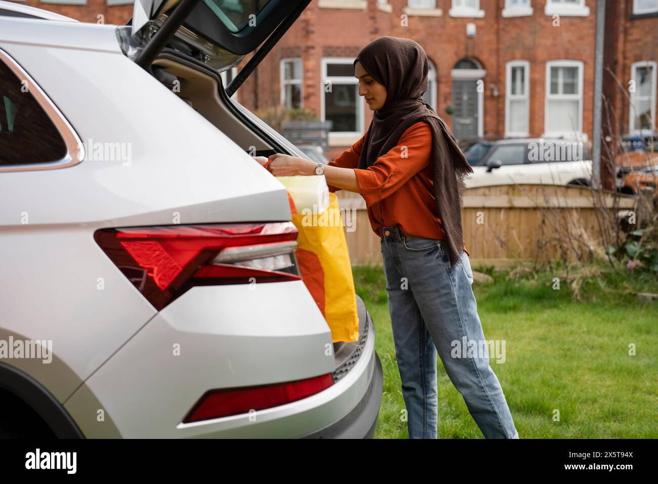 Woman wearing hijab unloading shopping bags from car trunk Stock Photo