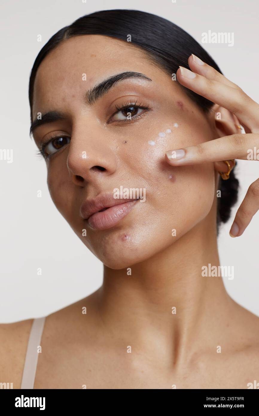 Studio shot of young woman applying cream on face Stock Photo