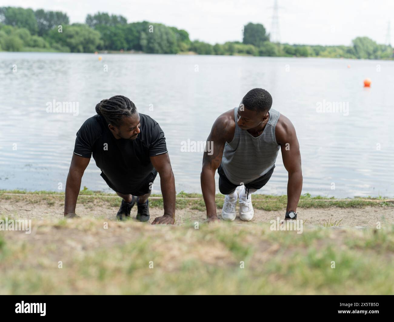 Two men doing push-ups in park by lake Stock Photo - Alamy
