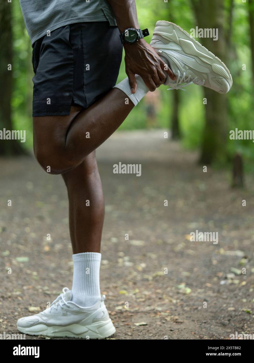 Man doing thigh stretch in forest Stock Photo