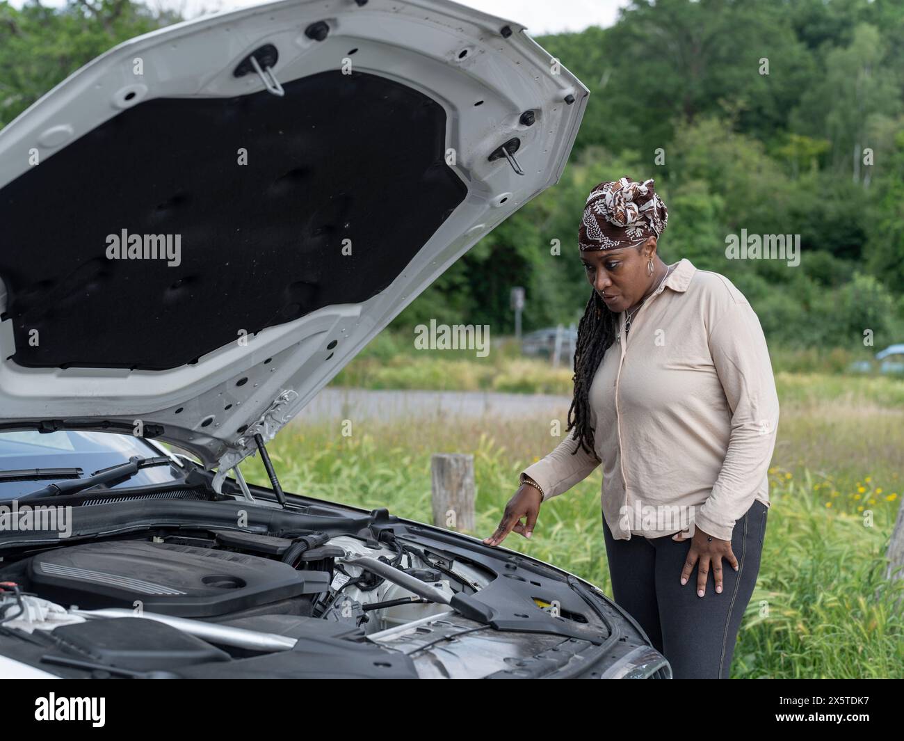 Woman standing over broken-down car Stock Photo