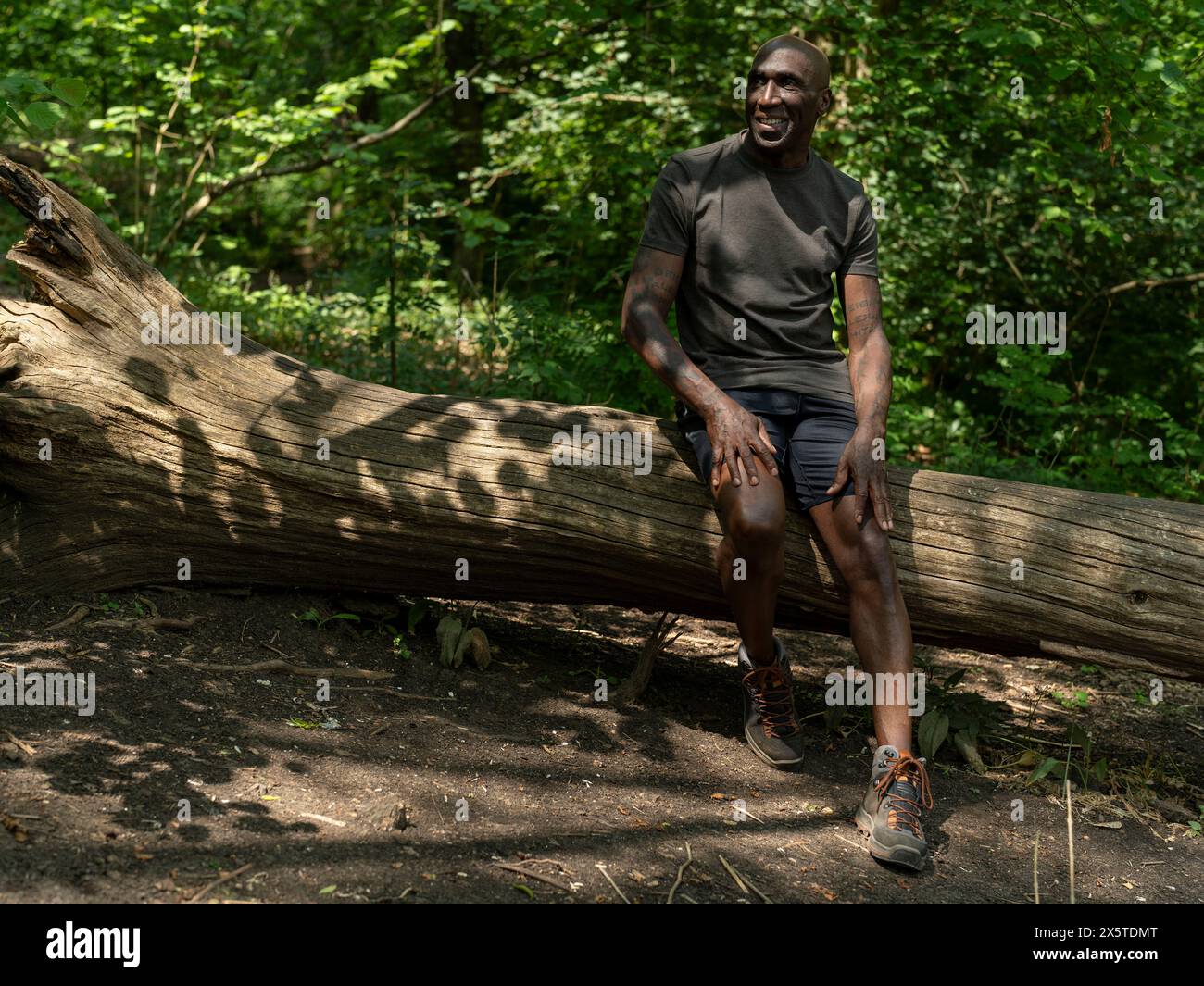 Mature man resting on log on hike Stock Photo