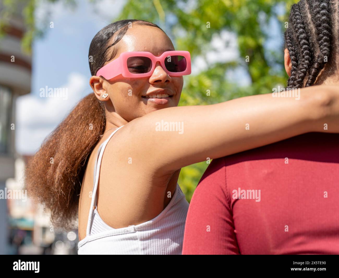 Portrait of smiling woman in sunglasses embracing friend on sunny day Stock Photo