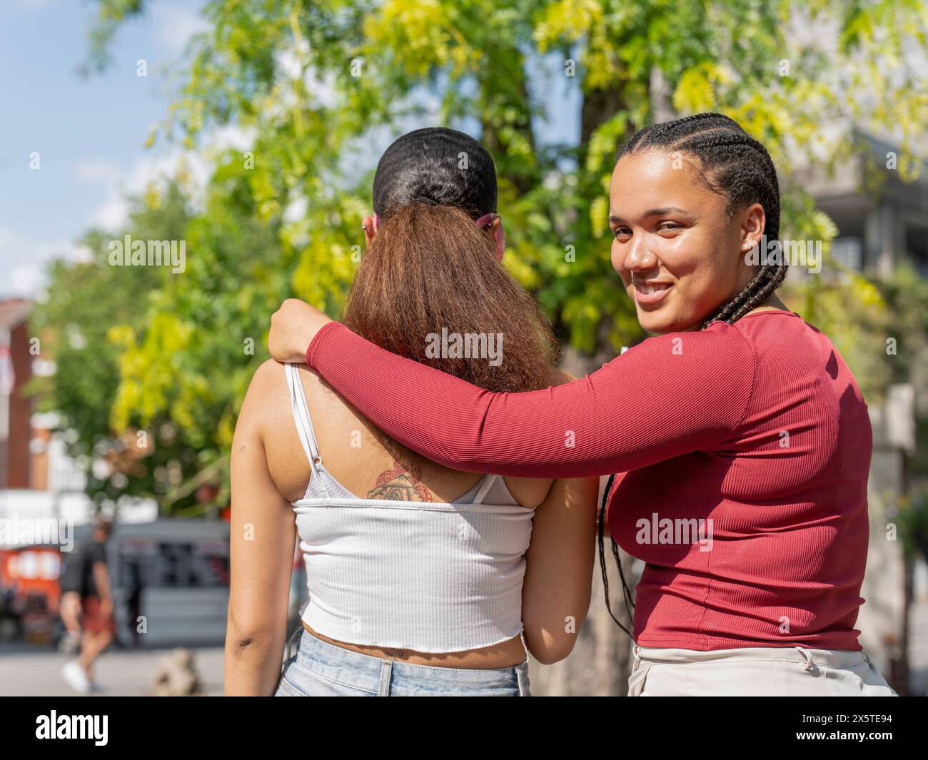 Portrait of smiling woman embracing friend on sunny day Stock Photo