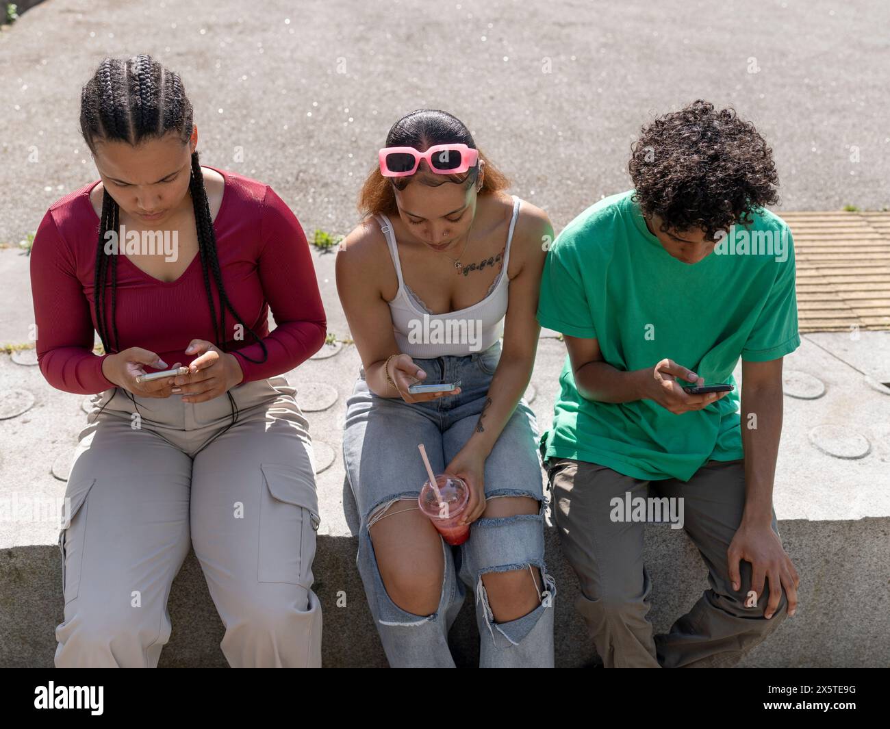Friends using smart phones while sitting on stone wall Stock Photo