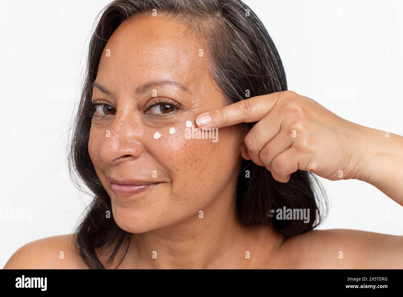 Studio portrait of smiling woman with dots of eye cream Stock Photo