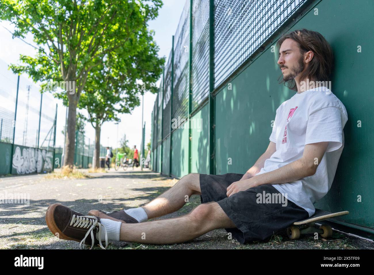 Young man sitting on skateboard outdoors Stock Photo