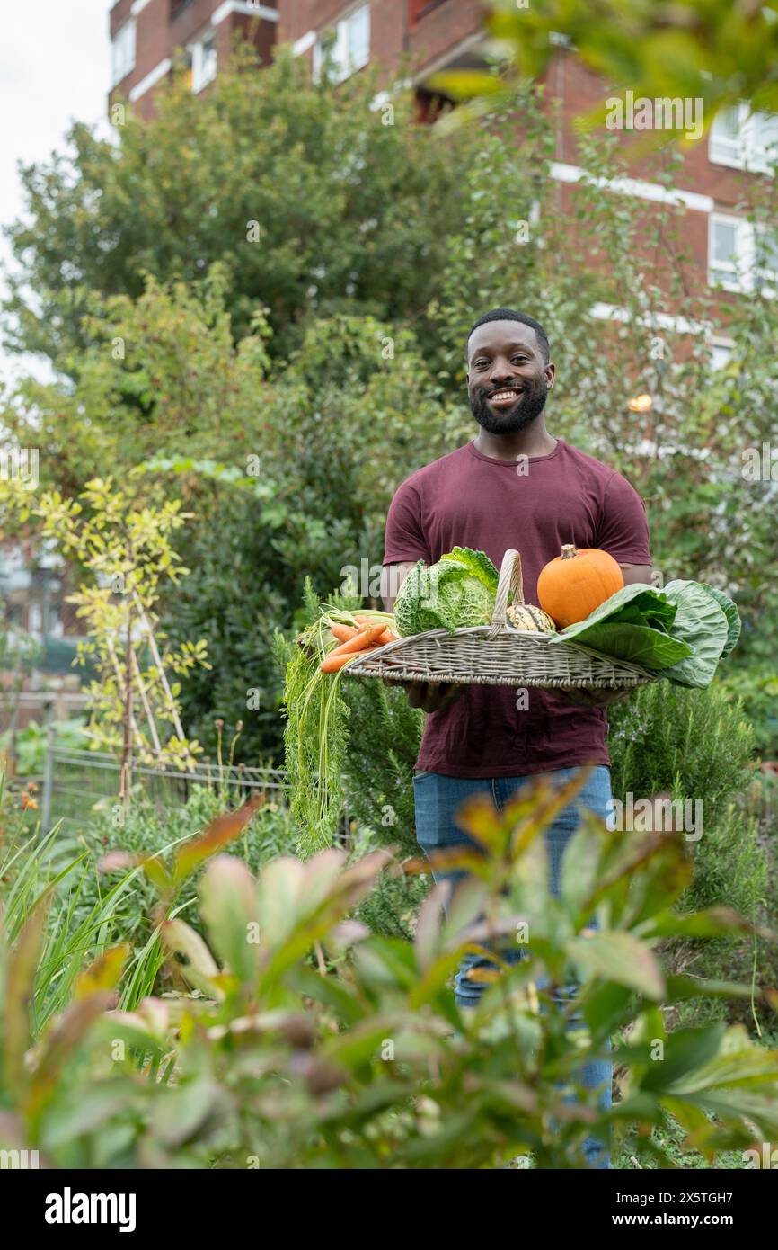 Portrait of smiling man holding basket with fresh vegetables in urban ...