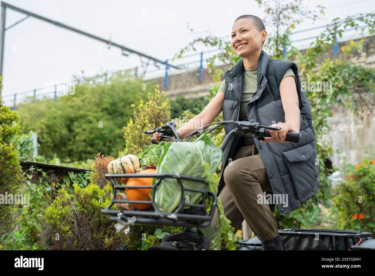 Smiling woman riding cargo electric trike loaded with homegrown vegetables Stock Photo