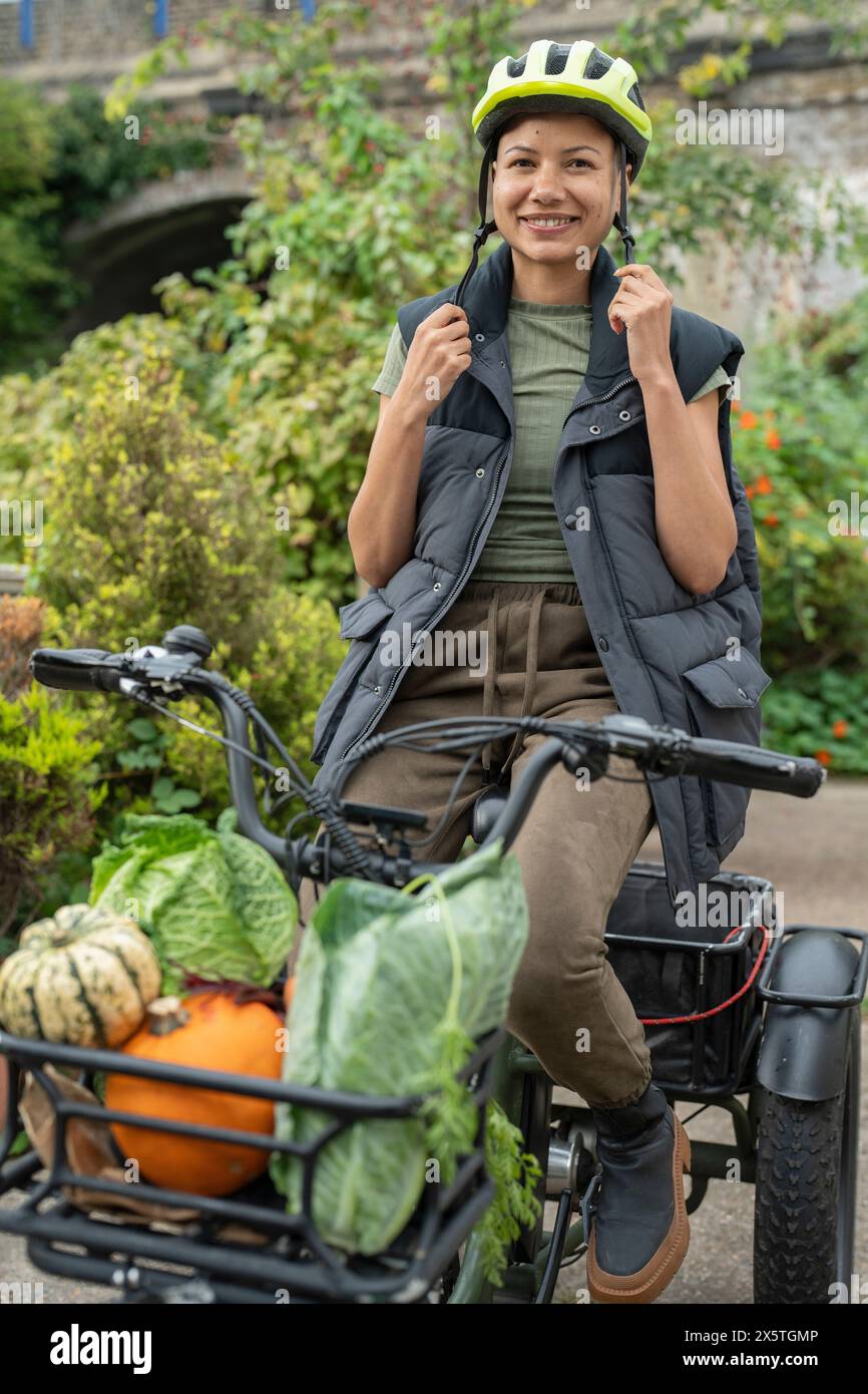 Smiling woman riding cargo electric trike loaded with homegrown vegetables Stock Photo