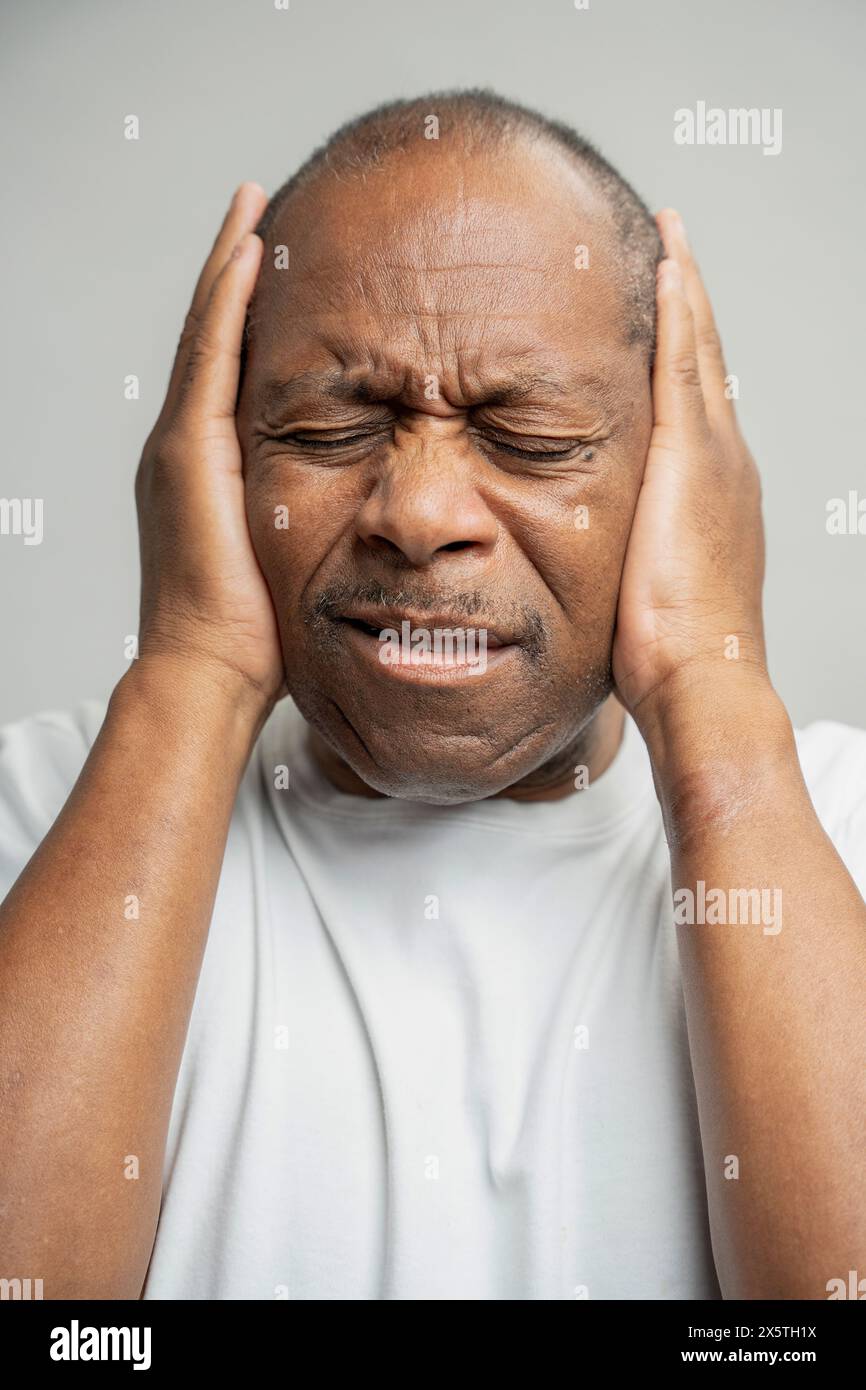 Portrait of man covering ears with hands against gray background Stock Photo