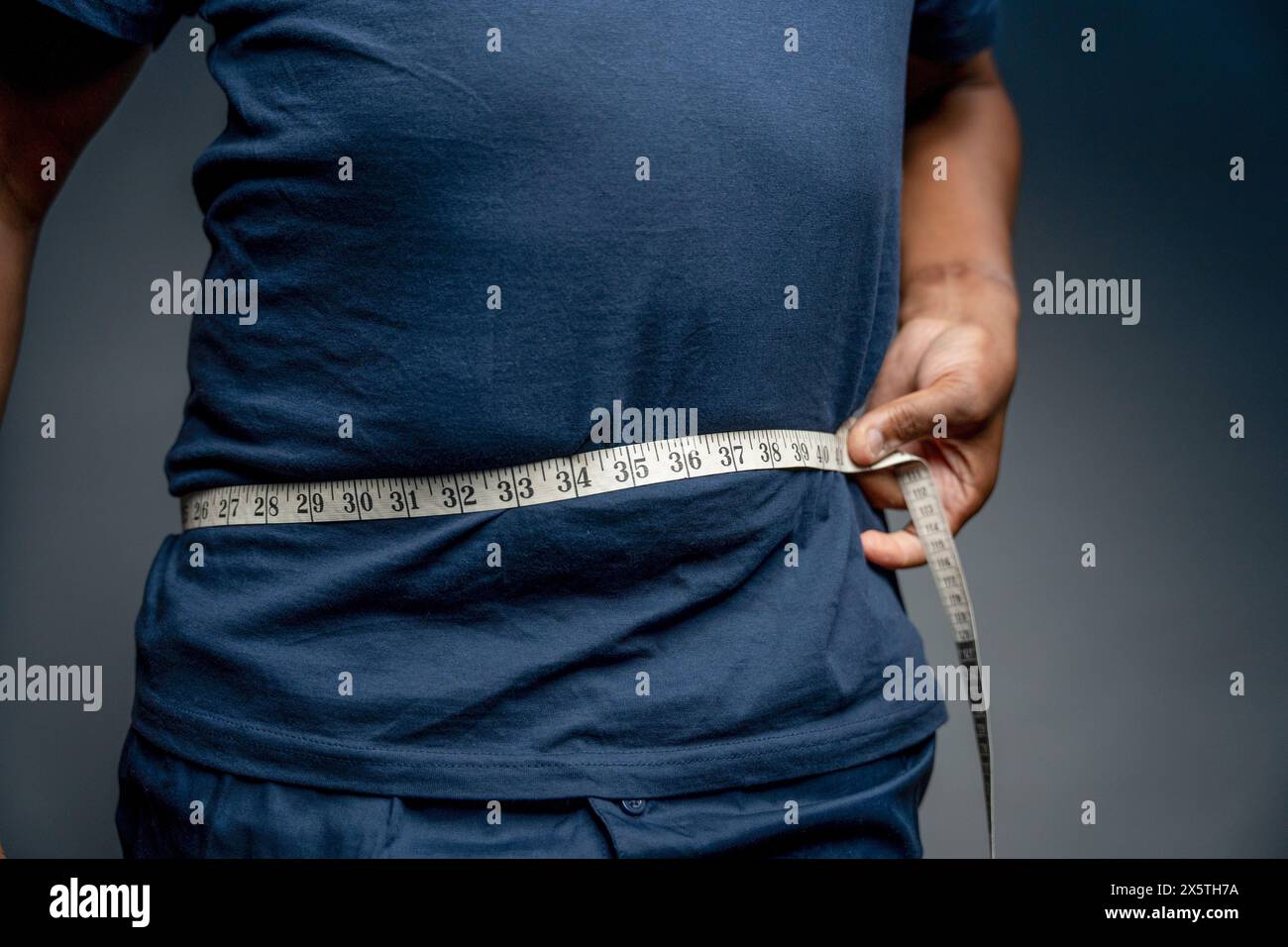 Senior man measuring waist against gray background Stock Photo