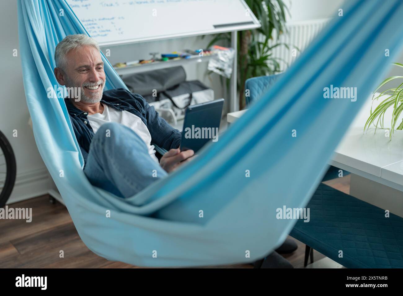 Smiling mature man lying in hammock and using digital tablet Stock Photo