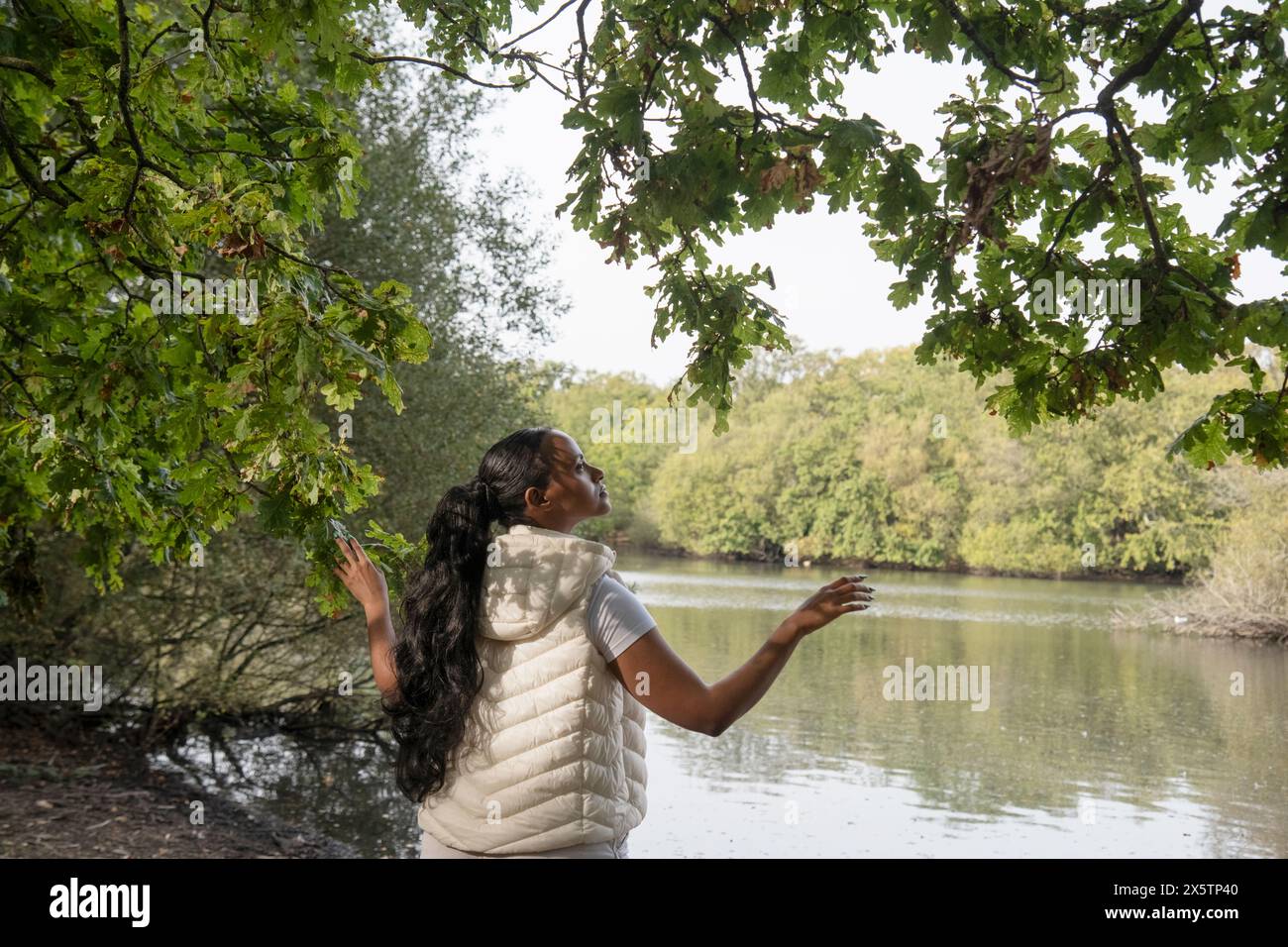 Rear view of woman standing by river with arms raised Stock Photo - Alamy
