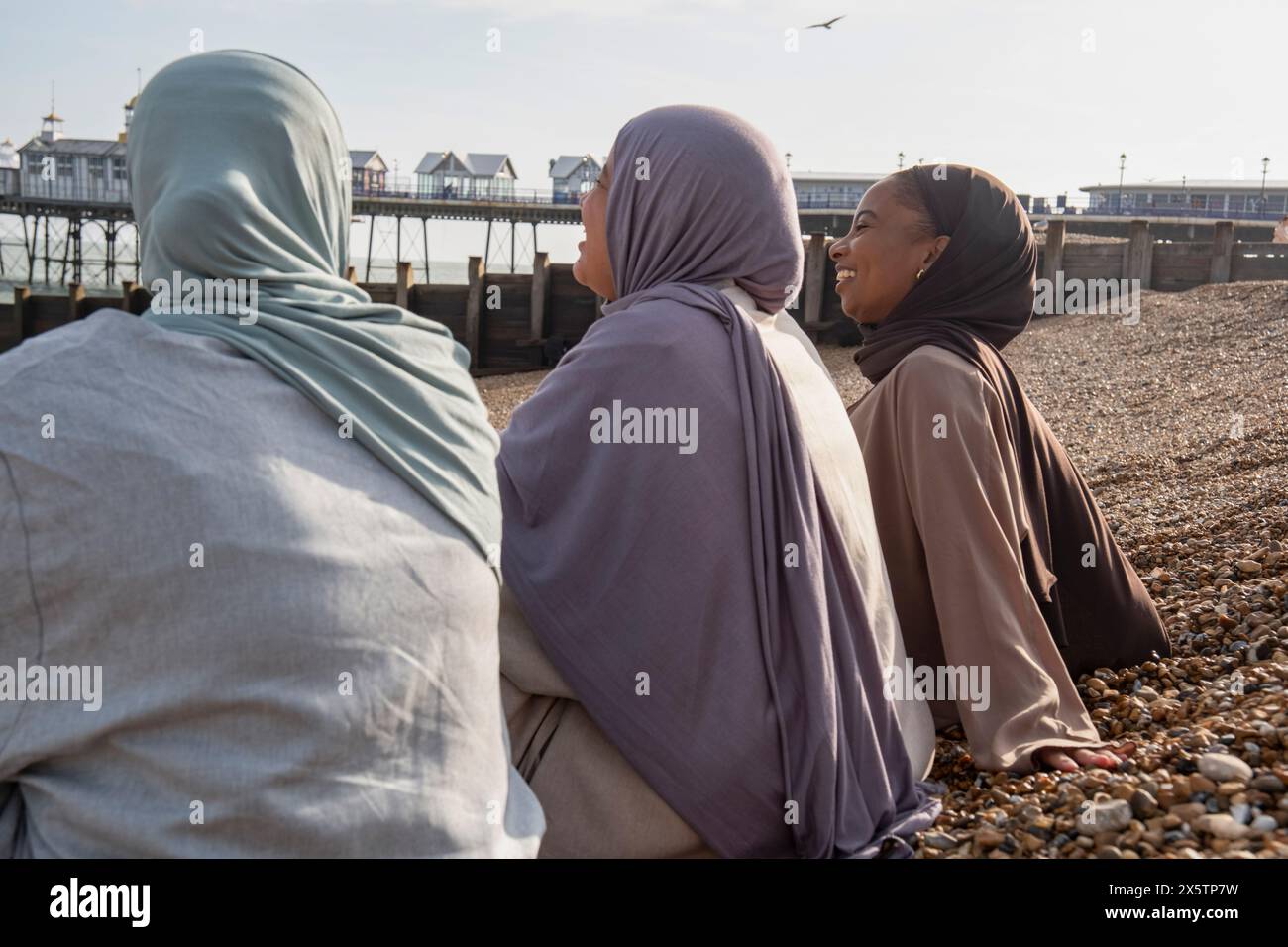 Three Muslim women sitting on beach on sunny day Stock Photo