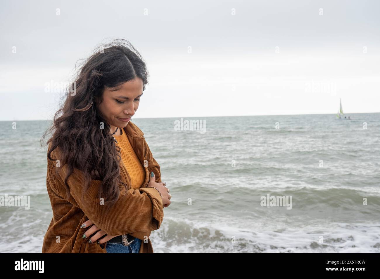 Thoughtful woman looking down while standing by sea on cloudy day Stock Photo