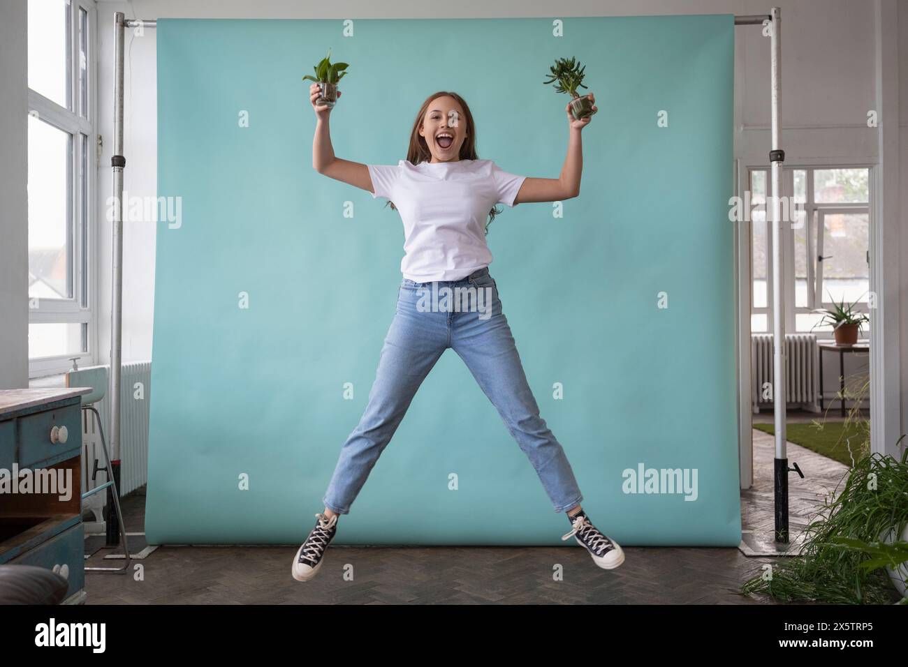 Studio portrait of teenage girl jumping with small potted plants in ...