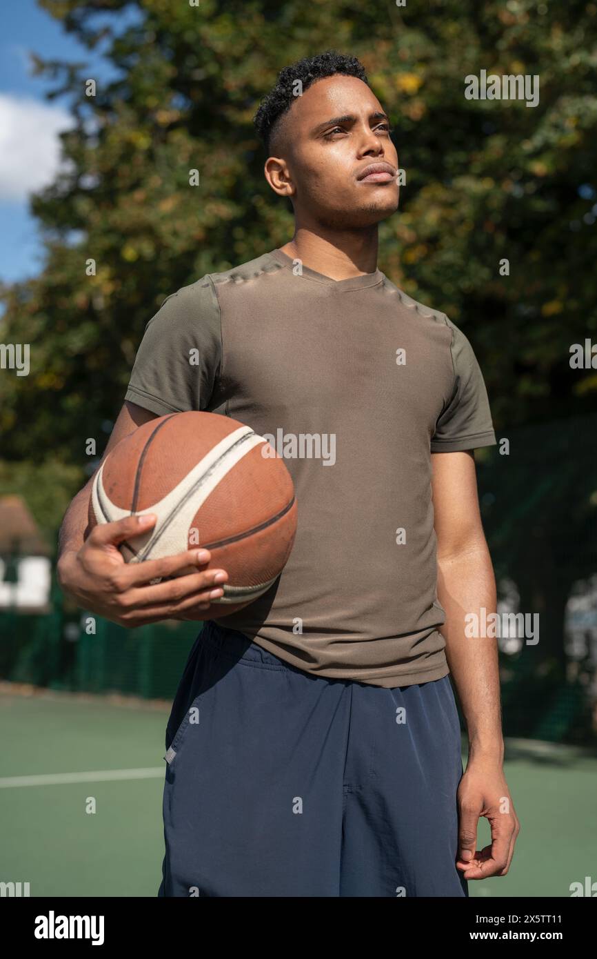 Portrait of pensive man with basketball ball in basketball court Stock Photo