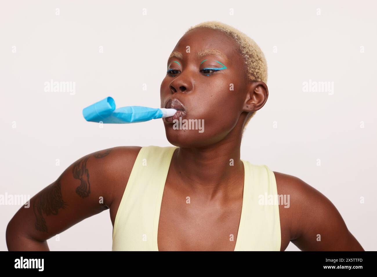 Woman with short white hair, holding party horn blower in mouth Stock Photo