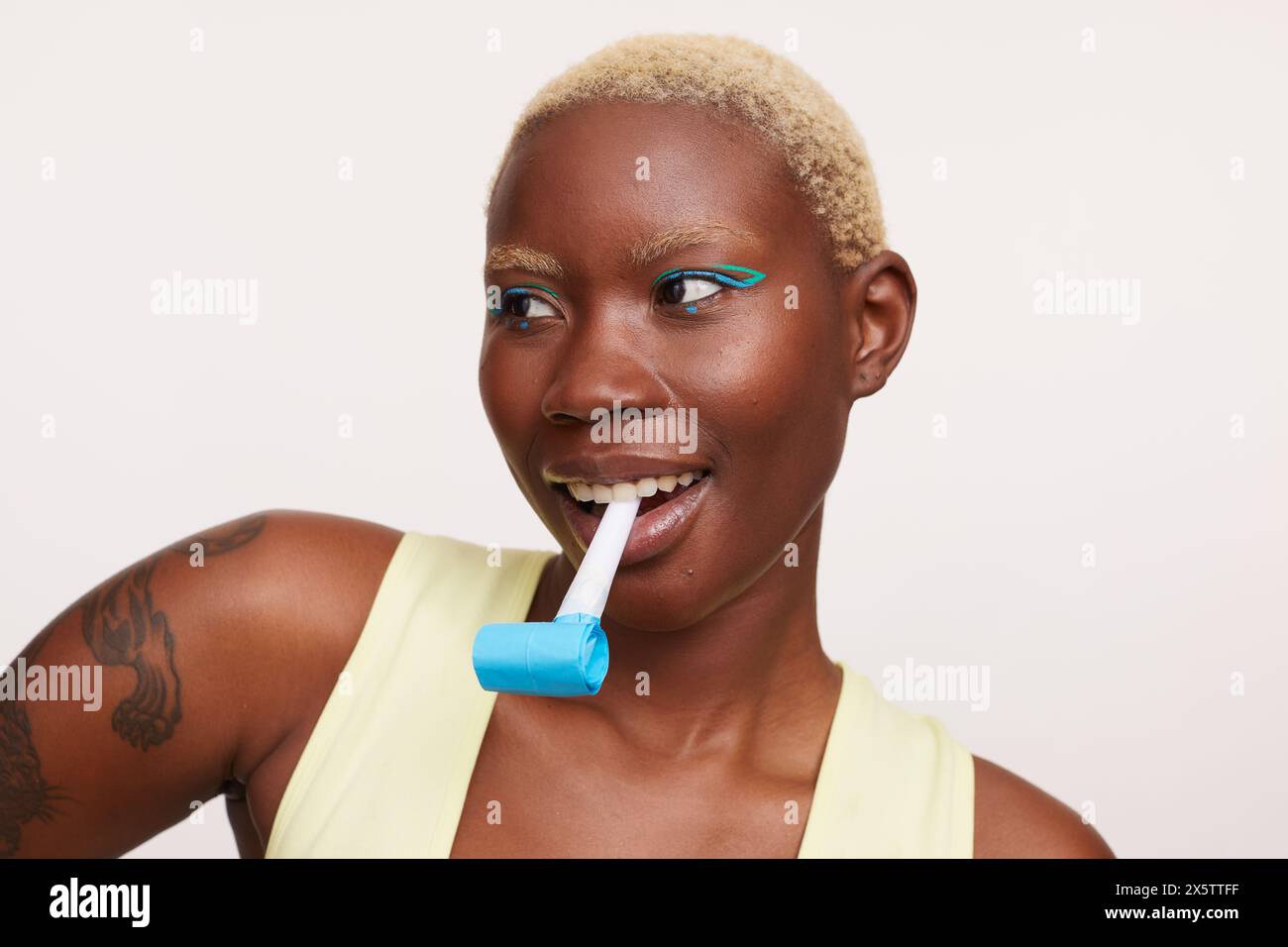 Woman with short white hair, holding party horn blower in mouth Stock Photo