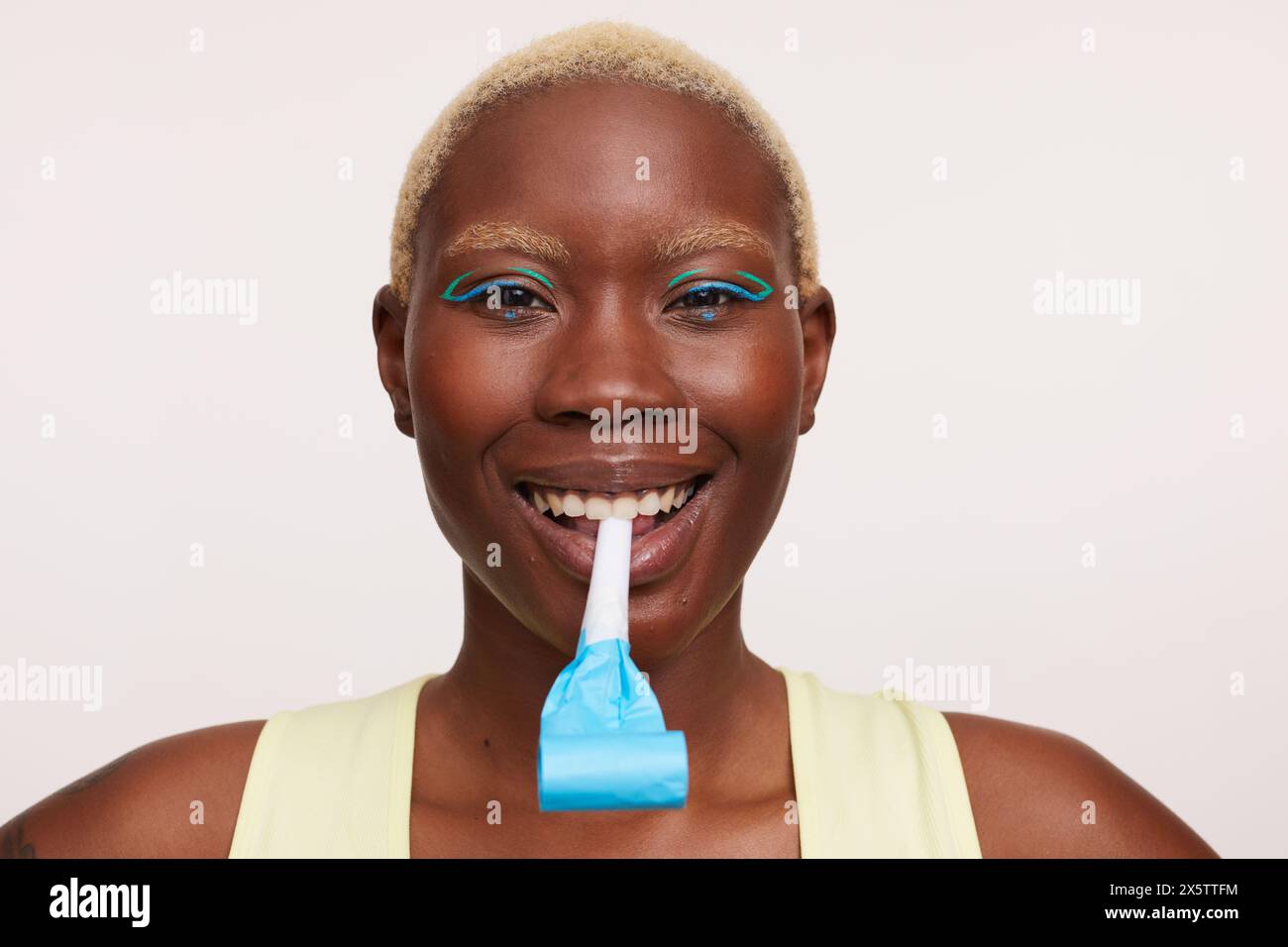 Smiling woman with short white hair, holding party horn blower in mouth Stock Photo