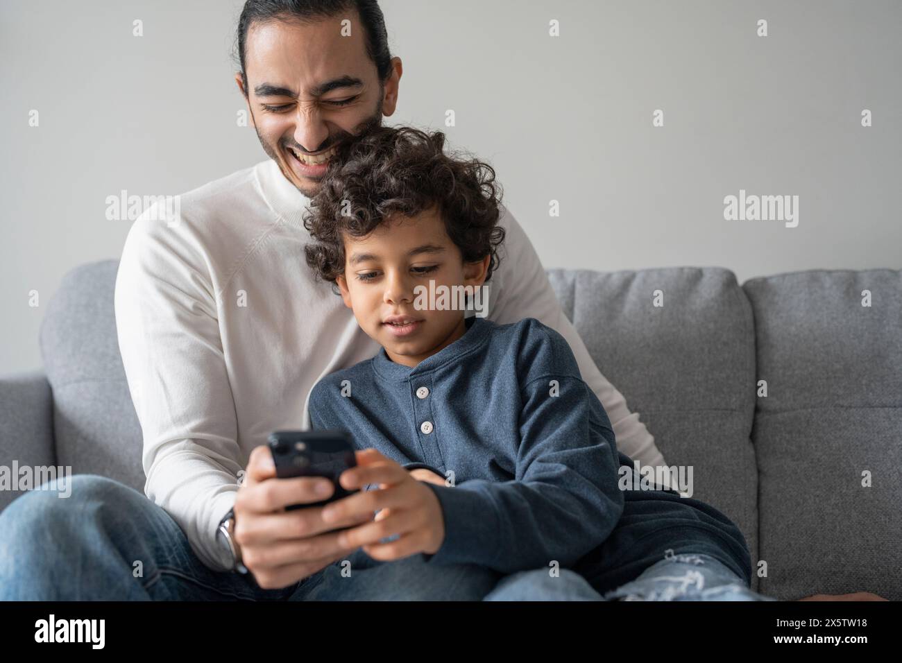 Father and son (6-7) using smart phone at home Stock Photo