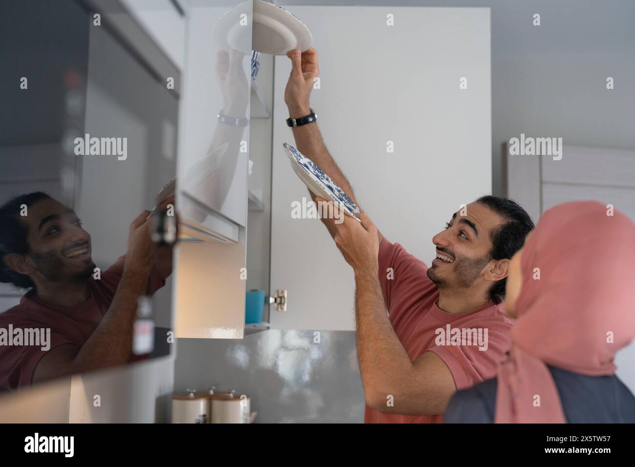 Smiling mid adult couple doing chores together in kitchen Stock Photo