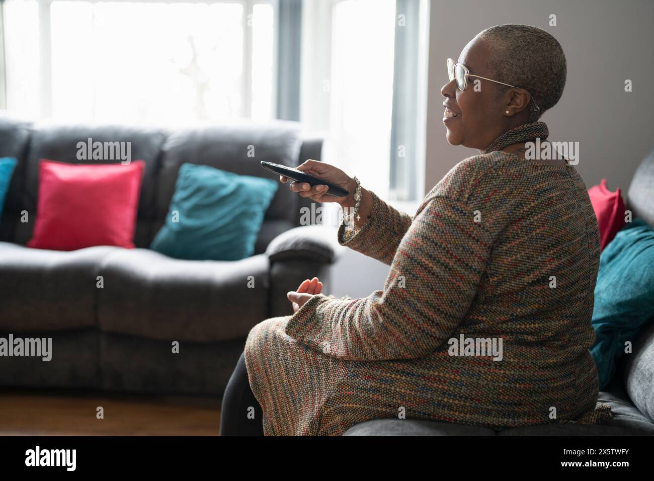 Mature woman sitting in living room and watching TV Stock Photo - Alamy
