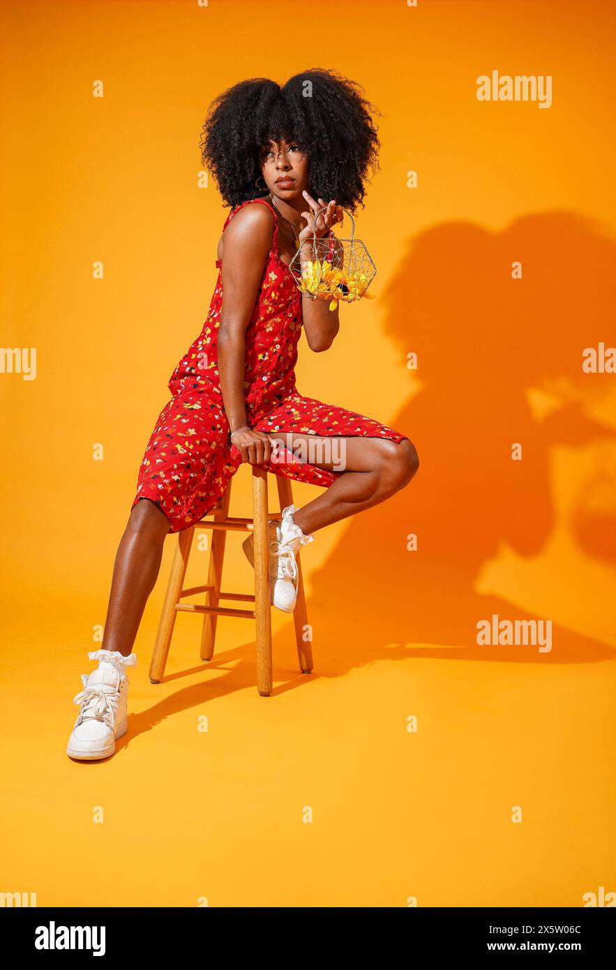 Studio portrait of stylish woman in red dress against yellow background ...