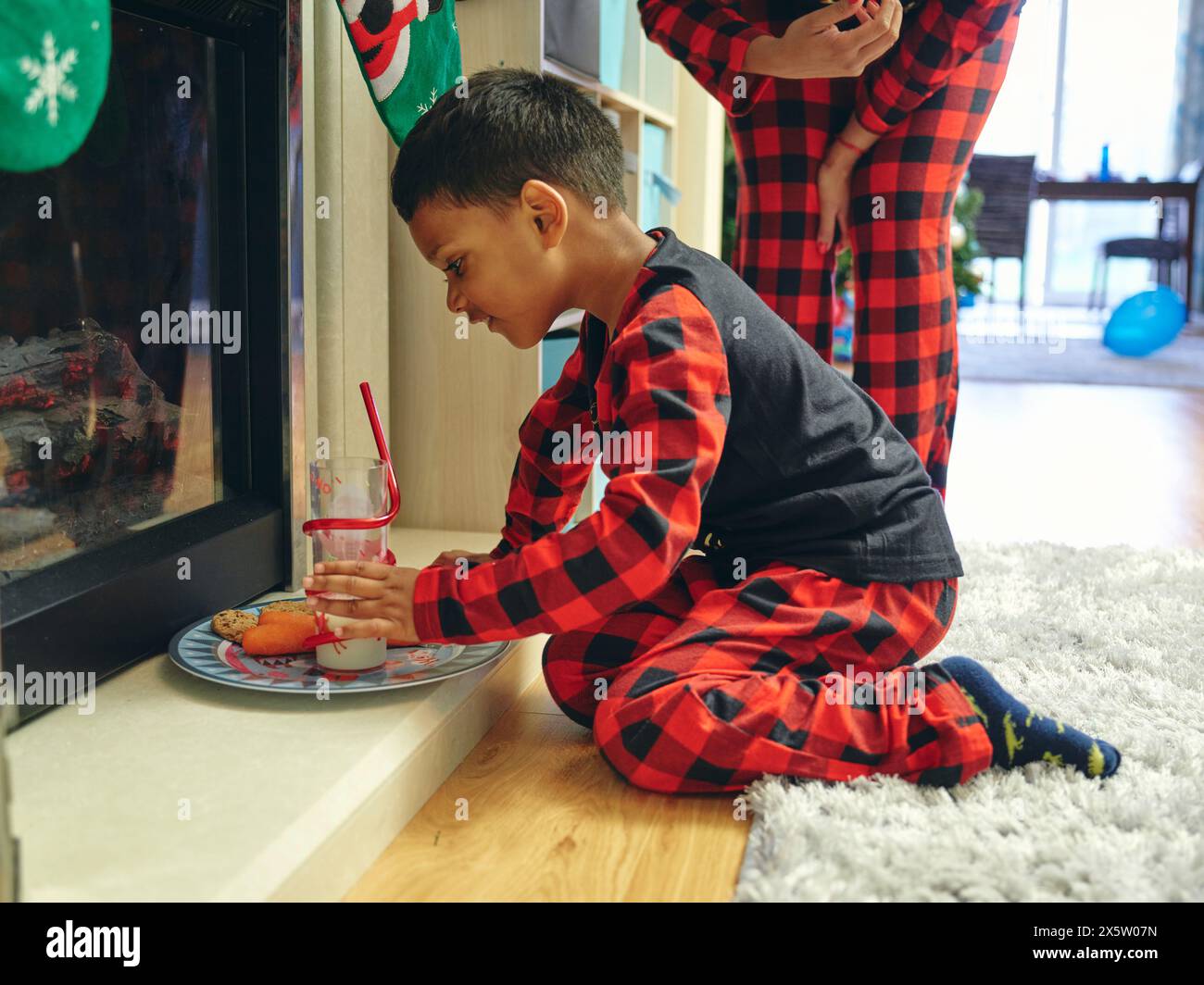 Mother and son leaving cookies and milk for Santa next to fireplace Stock Photo
