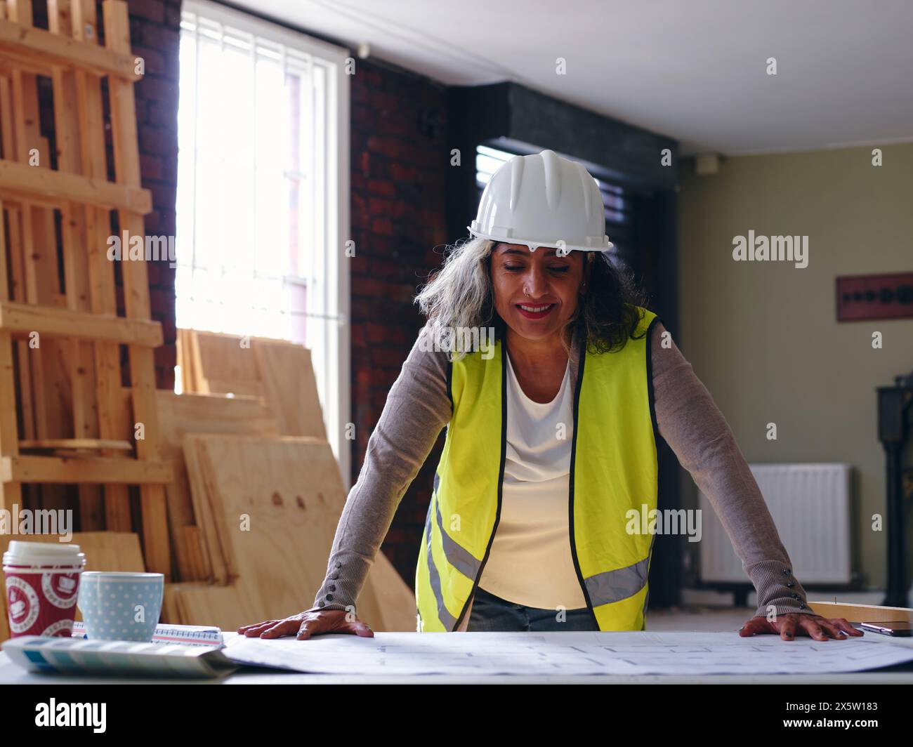 Woman in hardhat looking at blueprint Stock Photo - Alamy