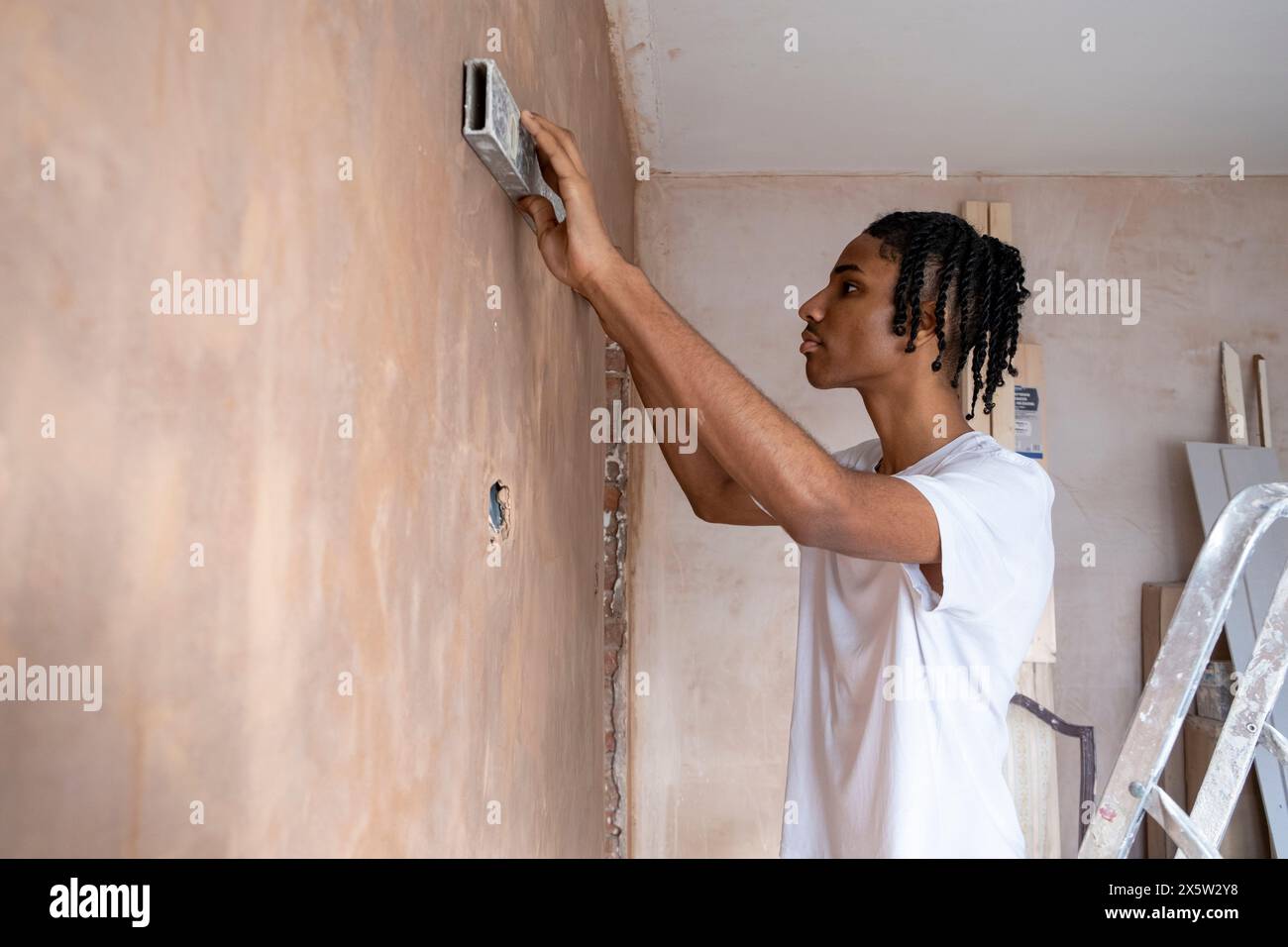Teenage boy using spirit level on wall Stock Photo - Alamy