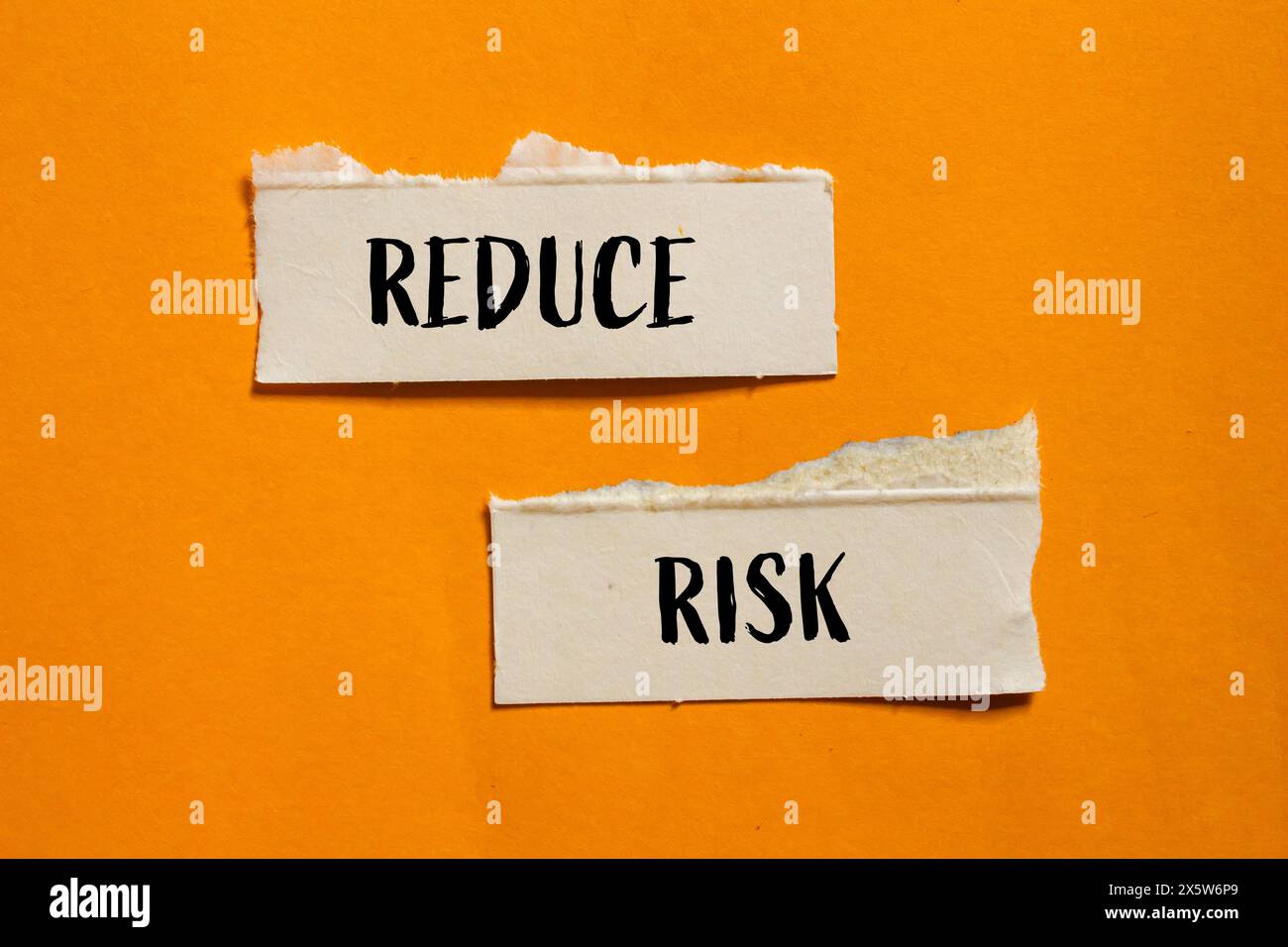 Reduce risk words written on ripped paper pieces with orange background. Conceptual reduce risk symbol. Copy space. Stock Photo