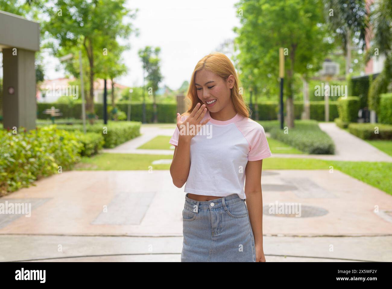 Asian girl with blonde hair smiling and looking down while laughing Stock Photo