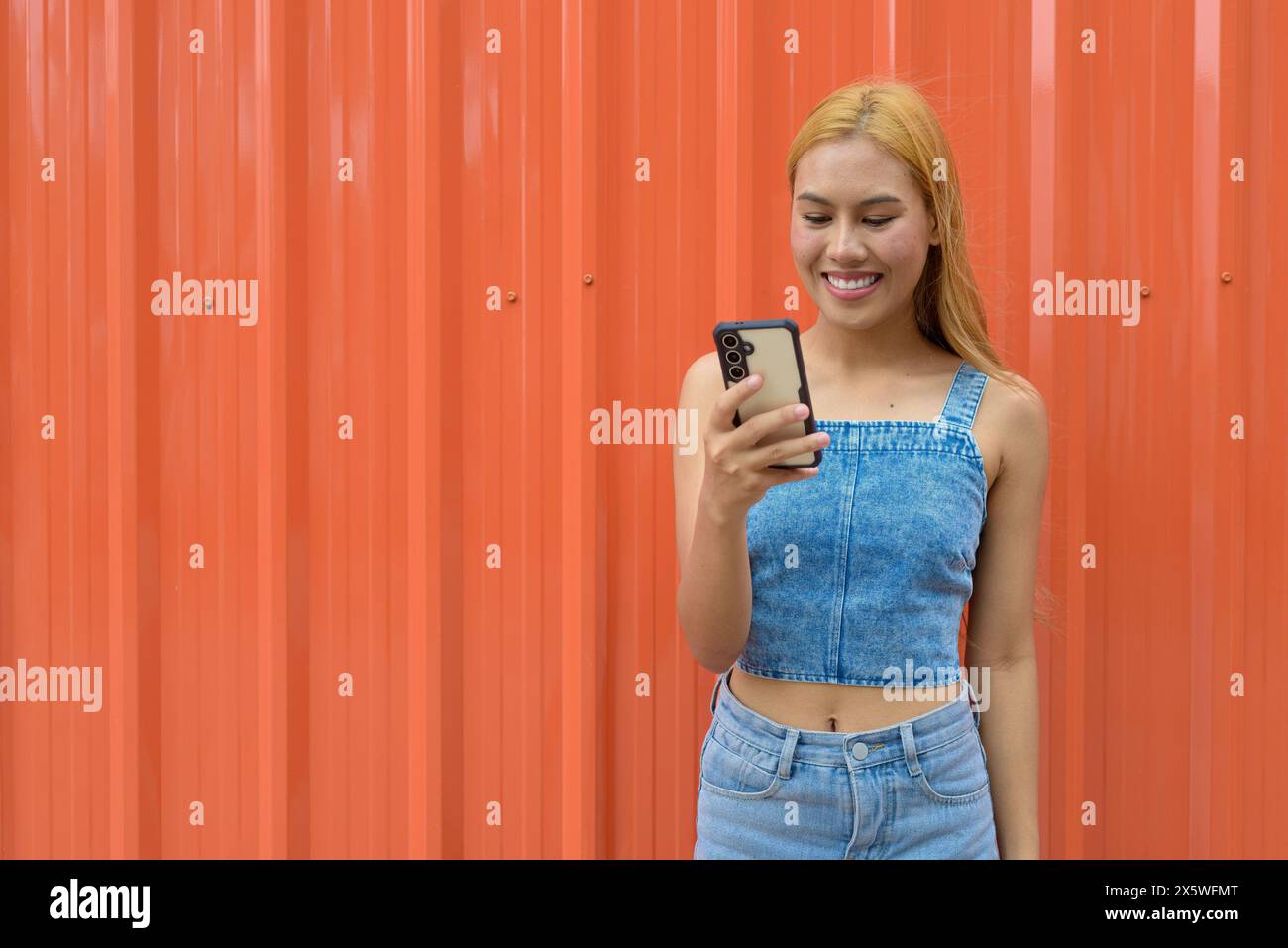 Beautiful Asian girl with blonde hair against orange background Stock Photo