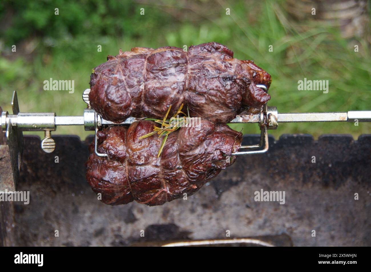 Beef with rosemary roasting on a spit outdoors. Stock Photo