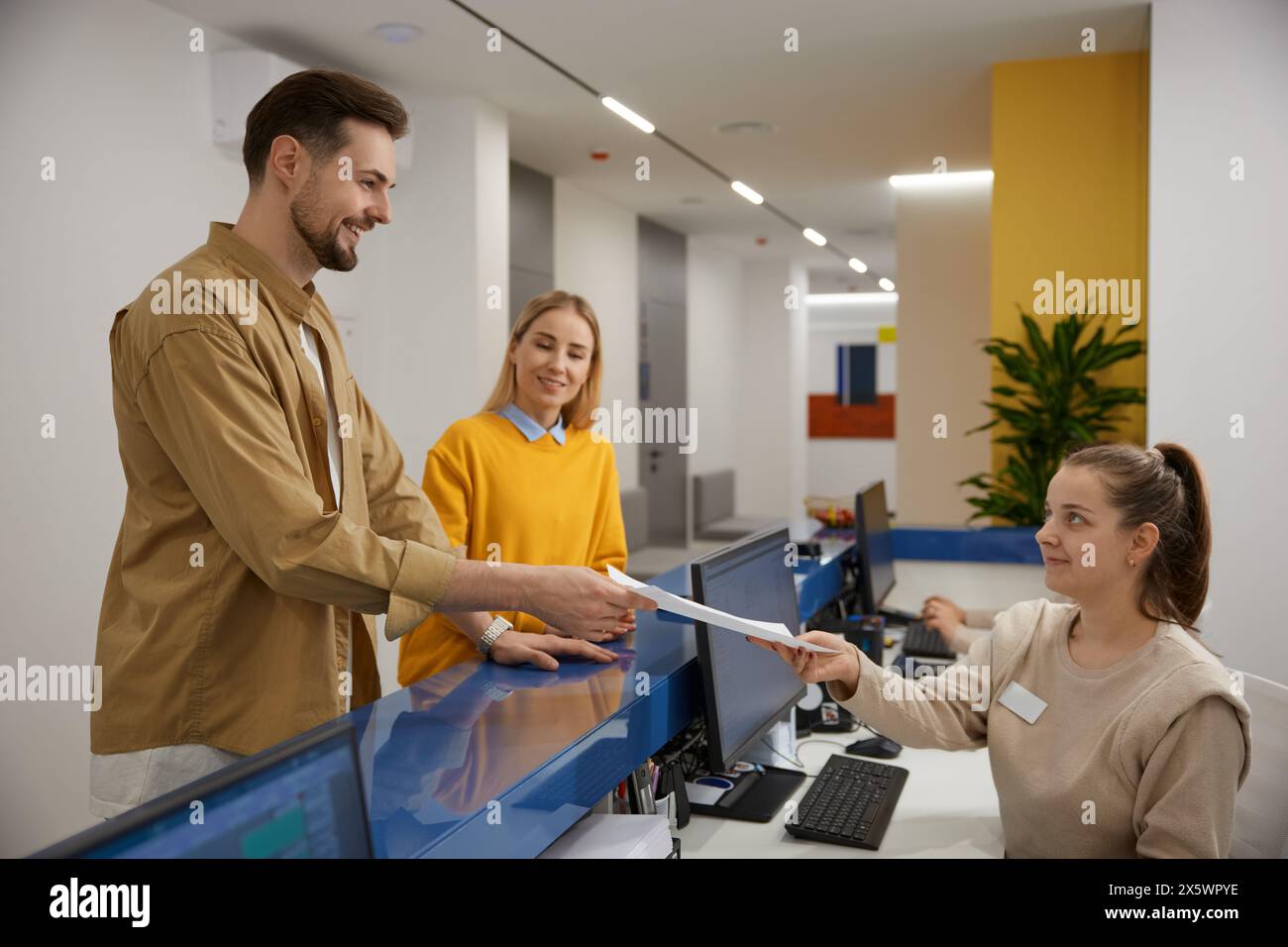 Man and woman couple signing document at modern clinic reception desk ...