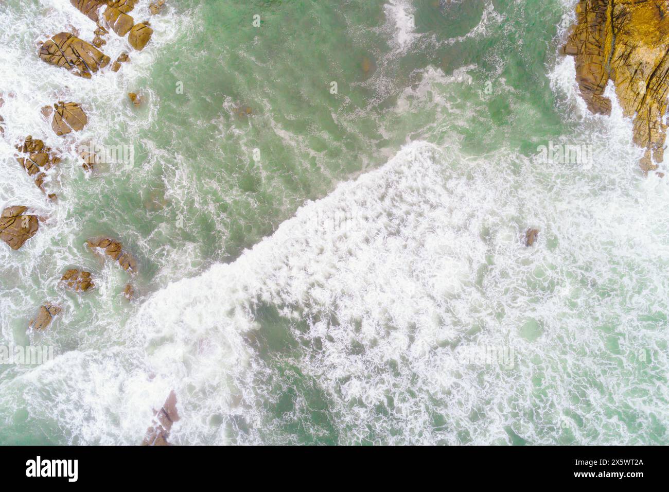 foam from waves breaking on a rocky coast, aerial overhead view with drone Stock Photo