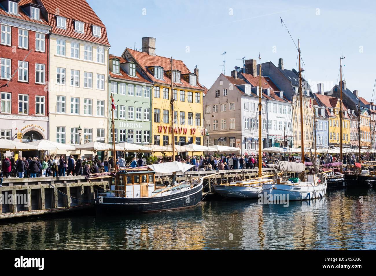 Copenhagen, Denmark - April 6, 2024: Crowded Nyhavn waterfront, canal and entertainment district in Copenhagen lined by brightly coloured historic tow Stock Photo