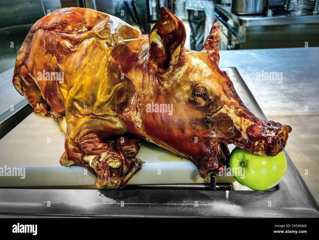 Roasted pig with a green apple in its mouth being served. Stock Photo