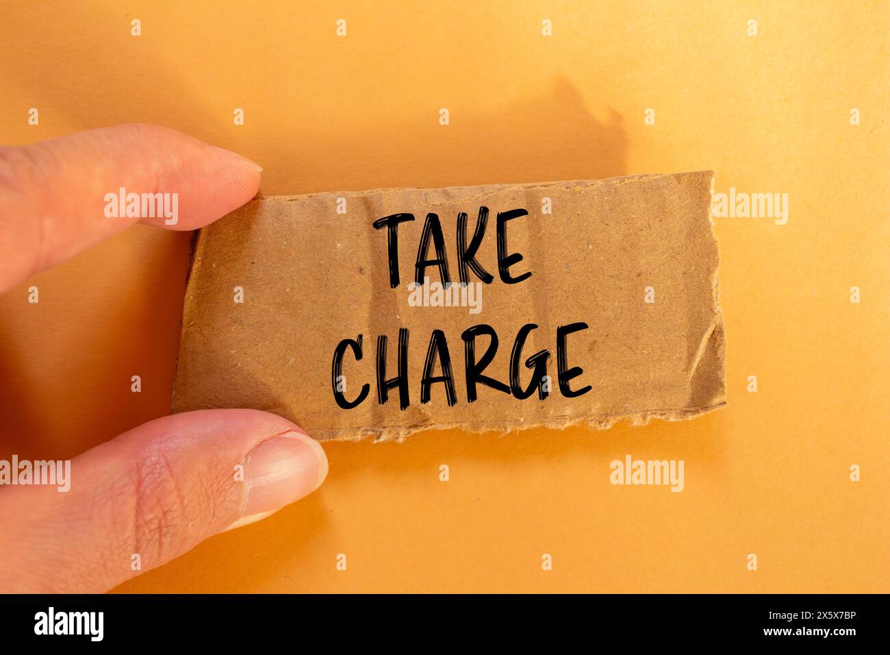 Take charge words written on ripped cardbaord paper with orange background. Conceptual take charge symbol. Copy space. Stock Photo
